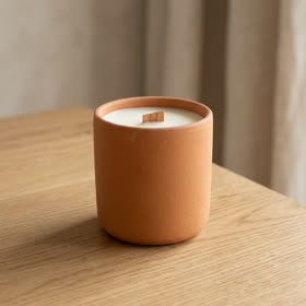 A terracotta soy candle with a wooden wick on a wooden table