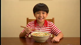 A boy in a striped shirt holding chopsticks over a bowl of noodles
